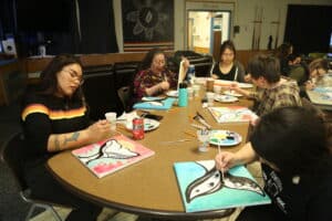 Art students paint colorful depictions of whale tales around a table at Ilisagvik College.