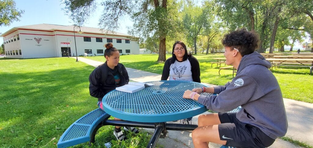 Three students at United Tribes Technical College sit at a table outdoors on a sunny day.