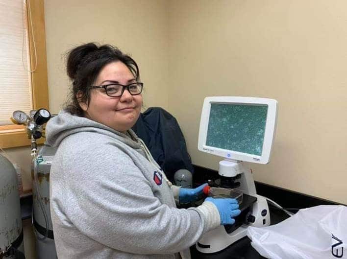 Rachel Matt sits near a microscope, smiling at the camera