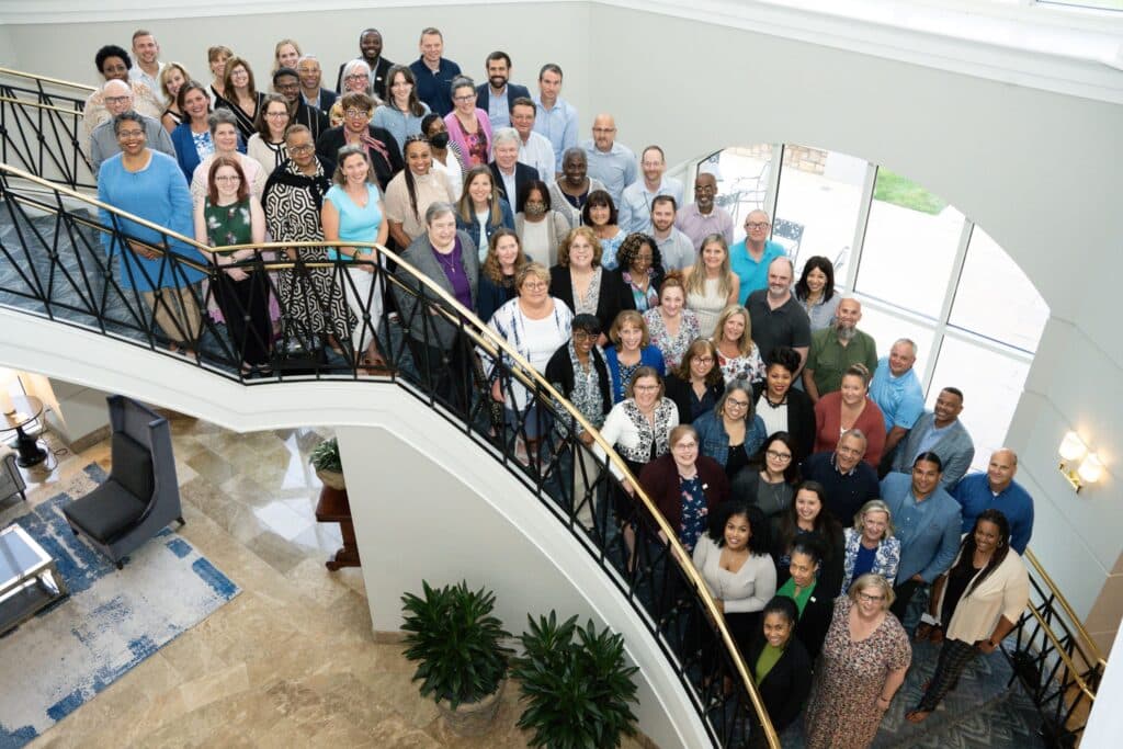 Dozens of college team members, ATD staff members, and ATD coaches gather for a group photo on the hotel stairs.