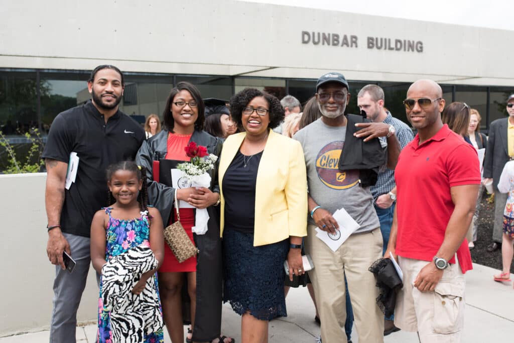 A new graduate poses with her family in front of the Dunbar Building at Roane State Community College