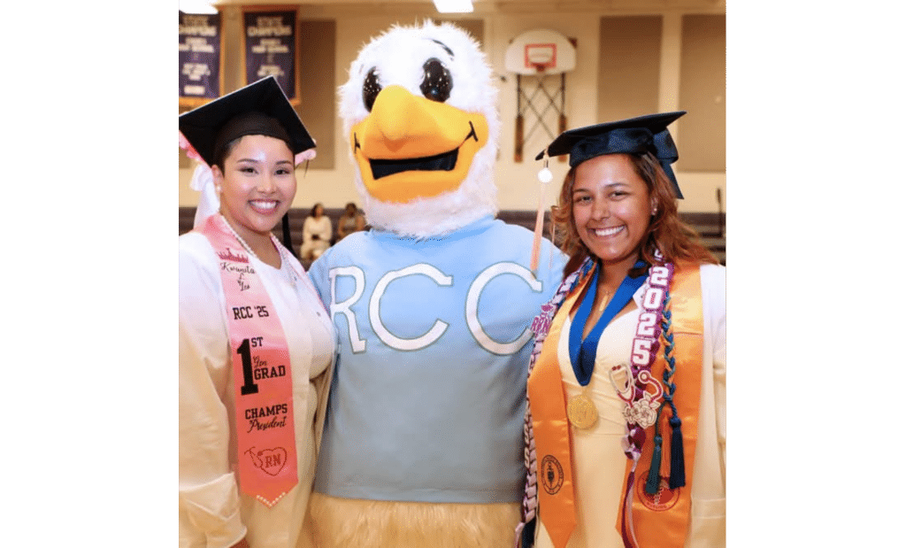 Two CHAMPS students at a graduation ceremony stand on either side of the RCC mascot