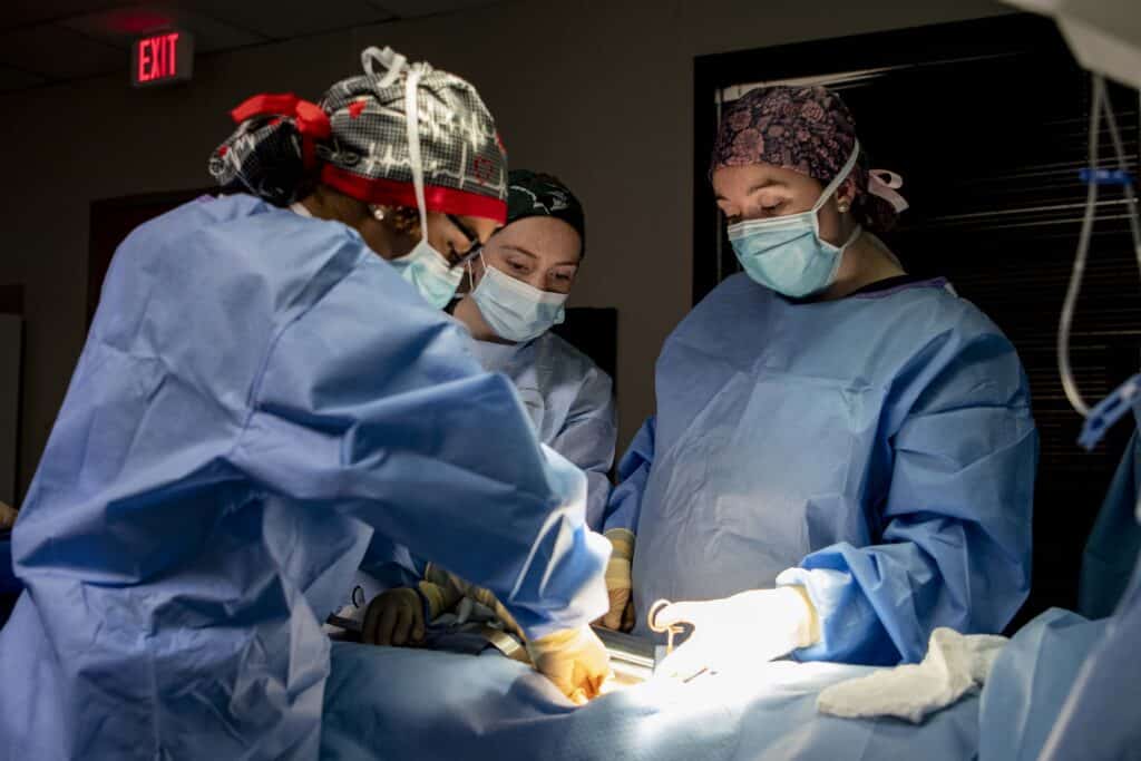 Three students in scrubs practice surgical nursing skills