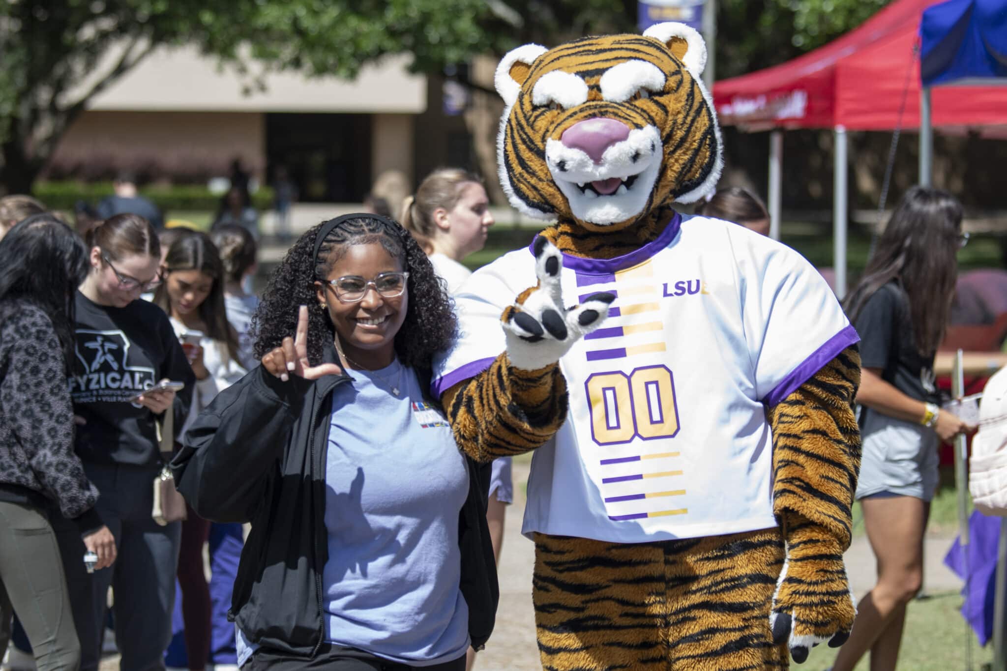 A young woman poses with the LSUE mascot, a tiger. Both hold their fingers in the shape of an L.